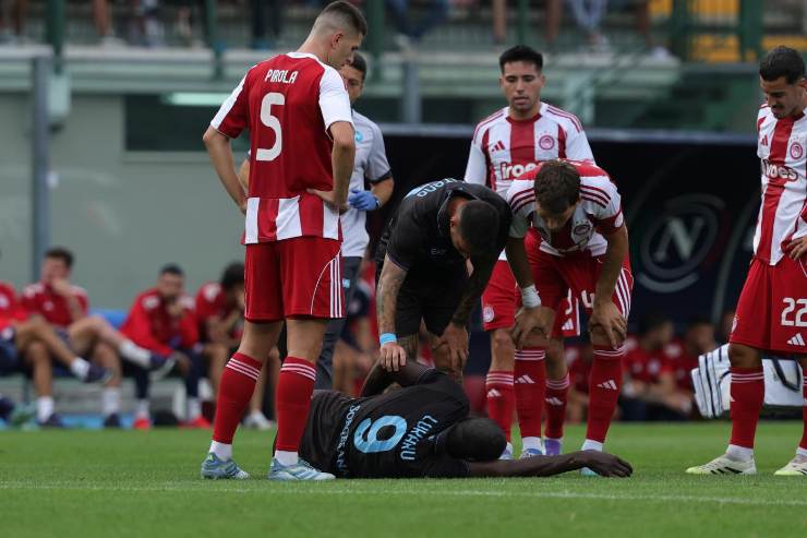 Romelu Lukaku a terra dolorante durante Napoli-Olympiacos 2025, circondato da compagni e avversari preoccupati.