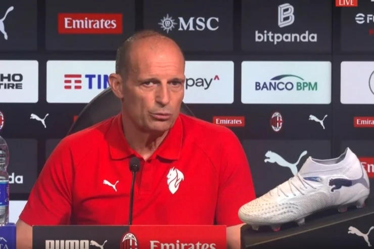Massimiliano Allegri in conferenza stampa con microfono, indossa la polo rossa del Milan davanti alle sponsorizzazioni