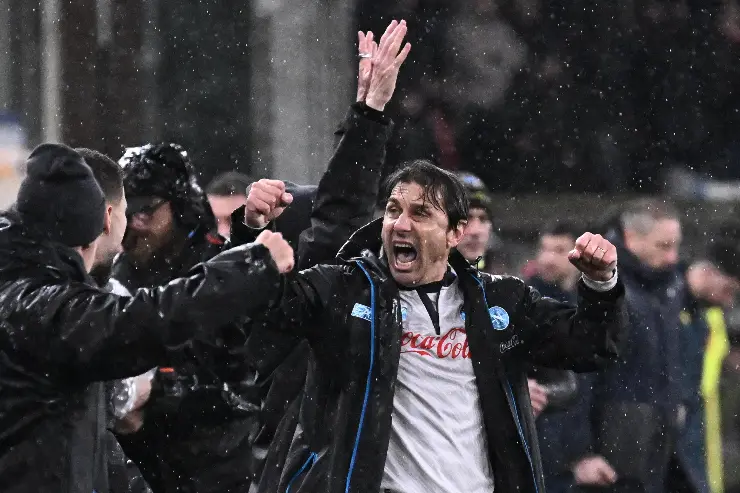 Antonio Conte esulta sotto la pioggia con il pugno alzato, indossa la tuta del Napoli con sponsor Coca-Cola