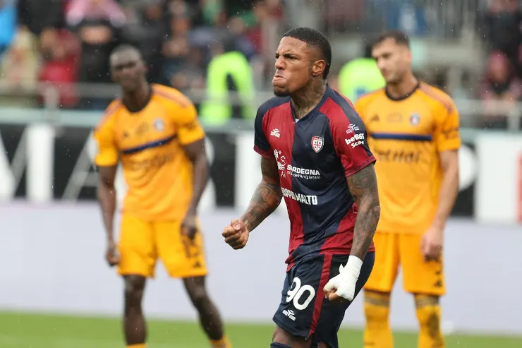 Folorunsho esulta durante una partita con la maglia del Cagliari, mentre giocatori in giallo sullo sfondo