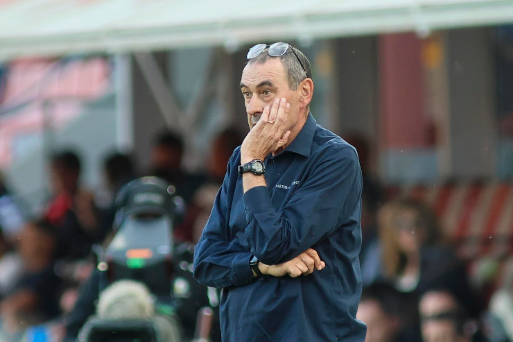 Maurizio Sarri in panchina durante una partita, con la mano al viso in atteggiamento concentrato
