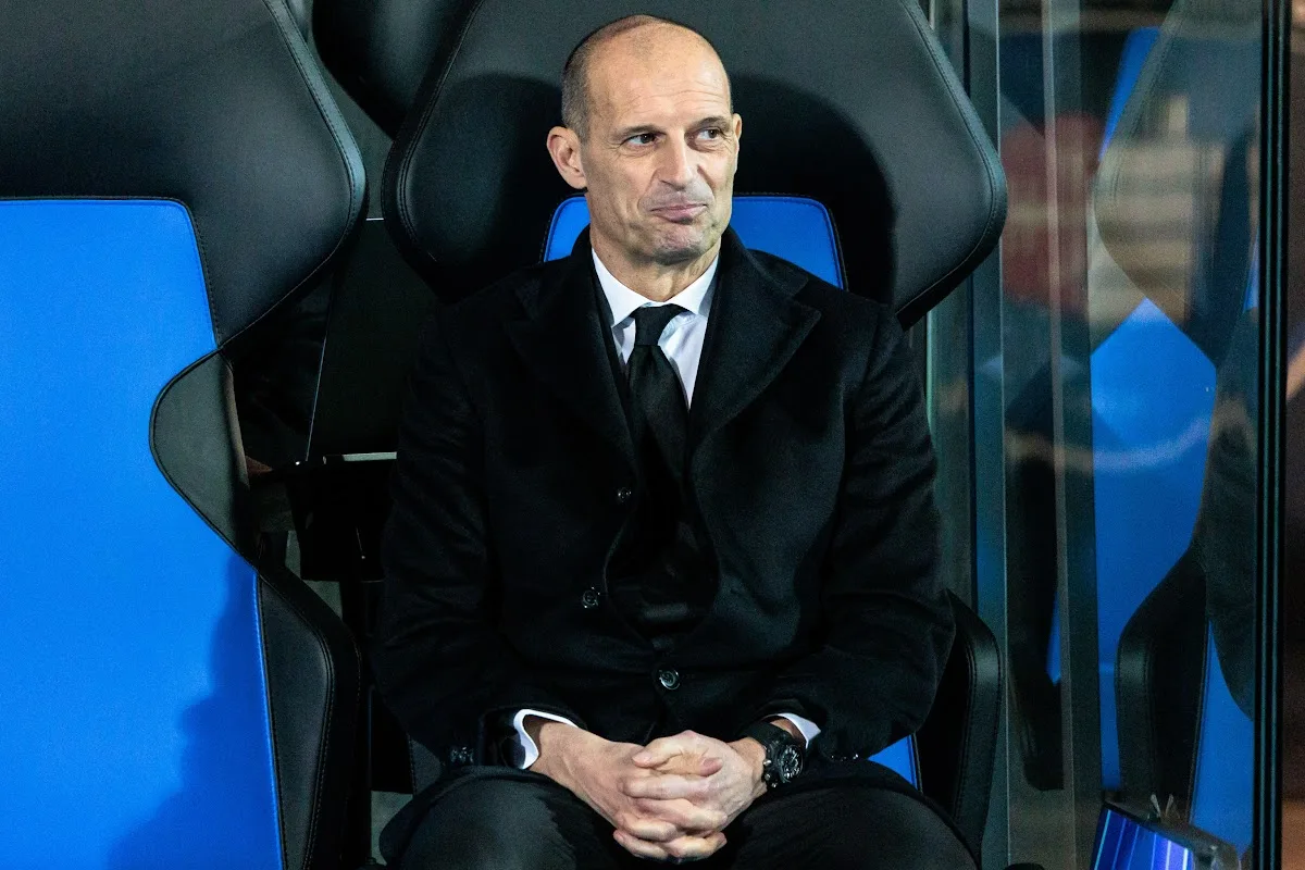 Massimiliano Allegri seduto in panchina, indossa abito nero e cravatta, concentrato durante una partita