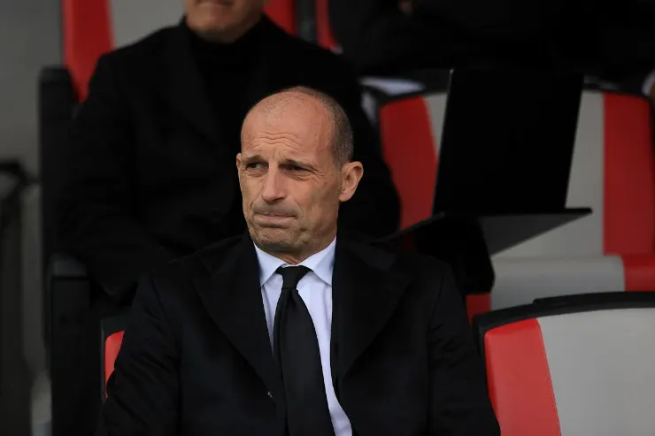 Massimiliano Allegri in panchina con espressione seria, indossa giacca nera e cravatta