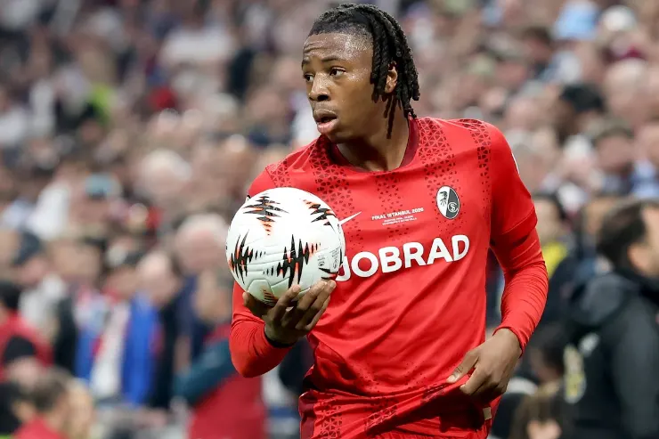 Giocatore con maglia rossa tiene il pallone durante una partita di calcio davanti al pubblico sugli spalti
