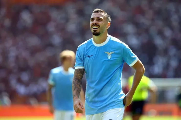 Mario Gila in maglia azzurra Lazio sorride durante la partita, sullo sfondo lo stadio pieno