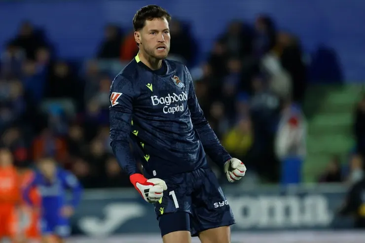 Remiro portiere della Real Sociedad durante una partita, in divisa blu scuro con guanti bianchi e rossi