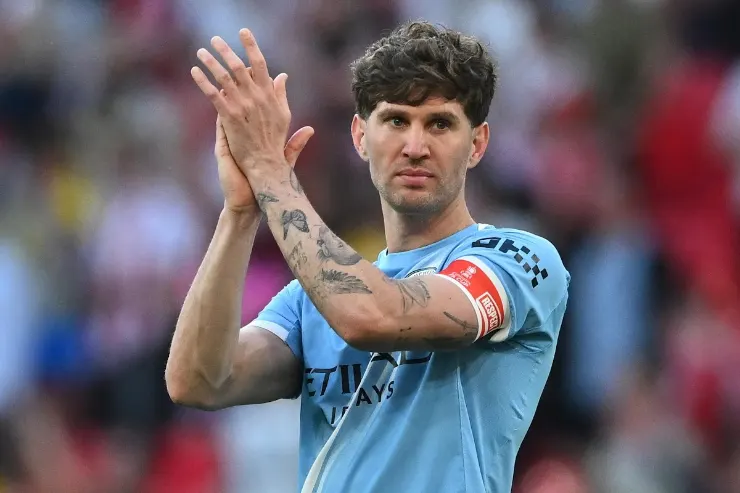 John Stones applaude durante una partita, indossa la fascia di capitano e la maglia azzurra