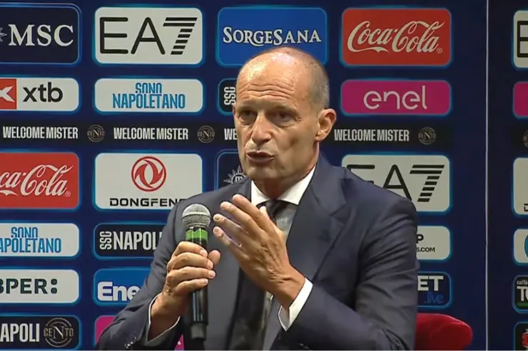 Allegri in conferenza stampa con microfono, dietro uno sfondo con sponsor del Napoli