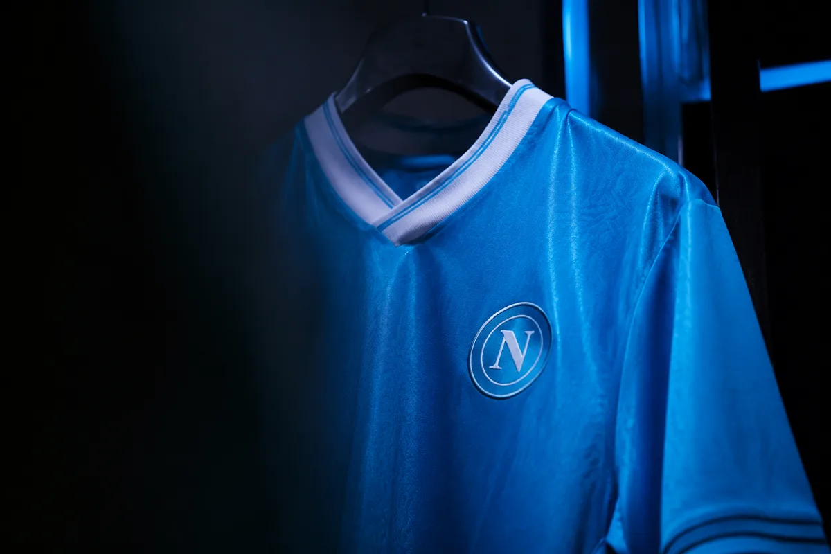 Maglia del Napoli blu appesa a un gancio, con logo della squadra in primo piano