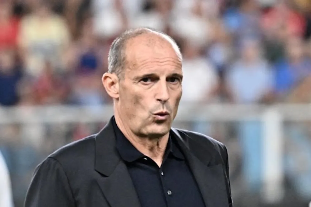 Allegri in panchina durante una partita di calcio, sullo sfondo lo stadio con tifosi