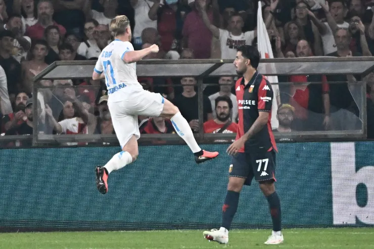 Giocatore in maglia bianca esulta durante una partita di calcio, avversario in maglia rosso-nera sullo sfondo