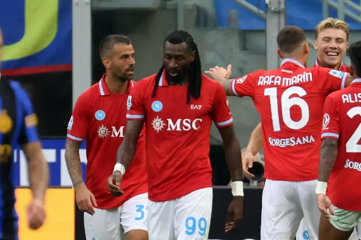 Giocatori del Napoli in maglia rossa celebrano insieme durante una partita, con Rafa Marin numero 16 in primo piano