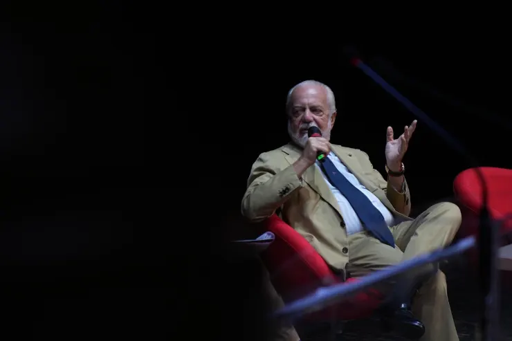 Aurelio De Laurentiis durante una conferenza, seduto in poltrona rossa, con microfono in mano mentre gesticola