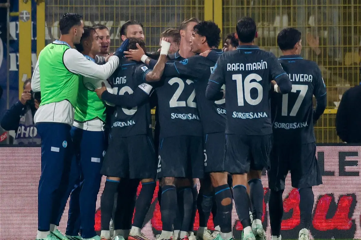 Giocatori del Napoli riuniti in un abbraccio di gruppo durante un'esultanza dopo un gol, con maglie blu scuro