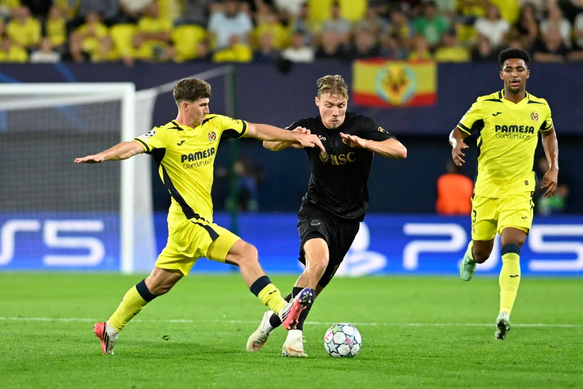 Giocatore del Napoli in maglia nera contrastato da due avversari del Villarreal in maglia gialla durante la partita