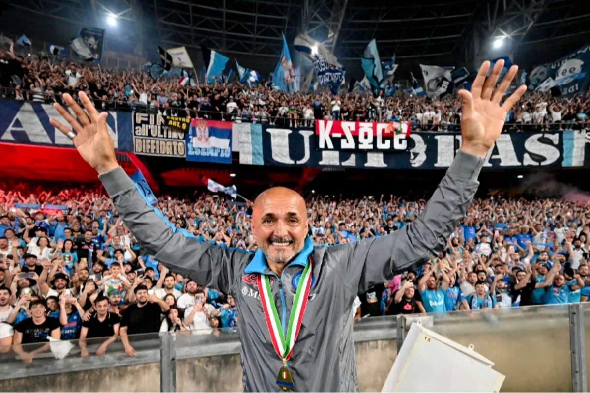 Luciano Spalletti con medaglia al collo alza le braccia esultando davanti ai tifosi del Napoli nello stadio